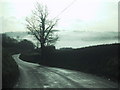 Road drops towards Sandford and a misty valley in EX17 4ED