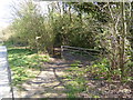 Footpath crosses farm track to stile by trees in RH10 4YY